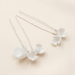 a pair of delicate white flower-shaped hair clips with a light beige background.