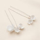 a pair of delicate white flower-shaped hair clips with a light beige background.