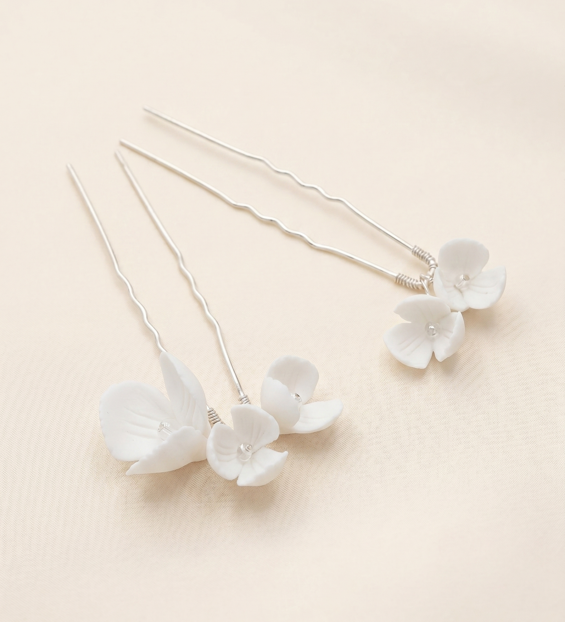 a pair of delicate white flower-shaped hair clips with a light beige background.