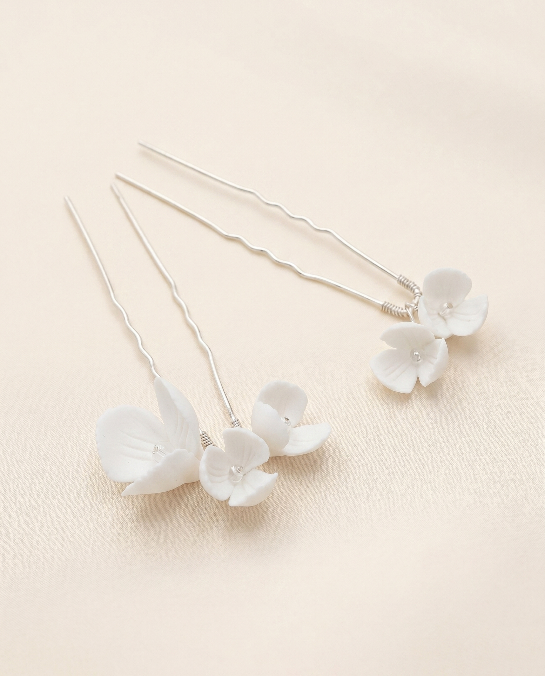 a pair of delicate white flower-shaped hair clips with a light beige background.