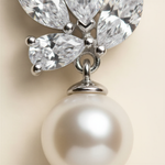 A close-up image of a pearl-like pendant with a silver clasp and a cluster of sparkling crystal gemstones attached to it.