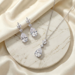A necklace with a pendant and earrings with a dangling design are displayed on a marble surface.