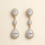 A pair of elegant gold earrings with three large pear-shaped gemstones set in a halo-like design.