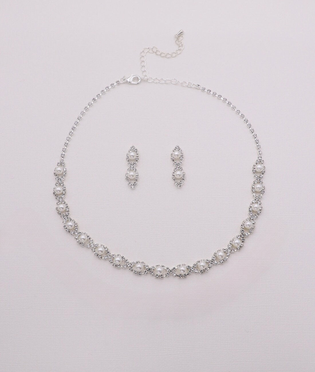 A necklace and earrings set made of silver and white pearls, arranged on a white background.