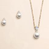 A necklace with a pendant and earrings made of pearls and diamonds against a light beige background.