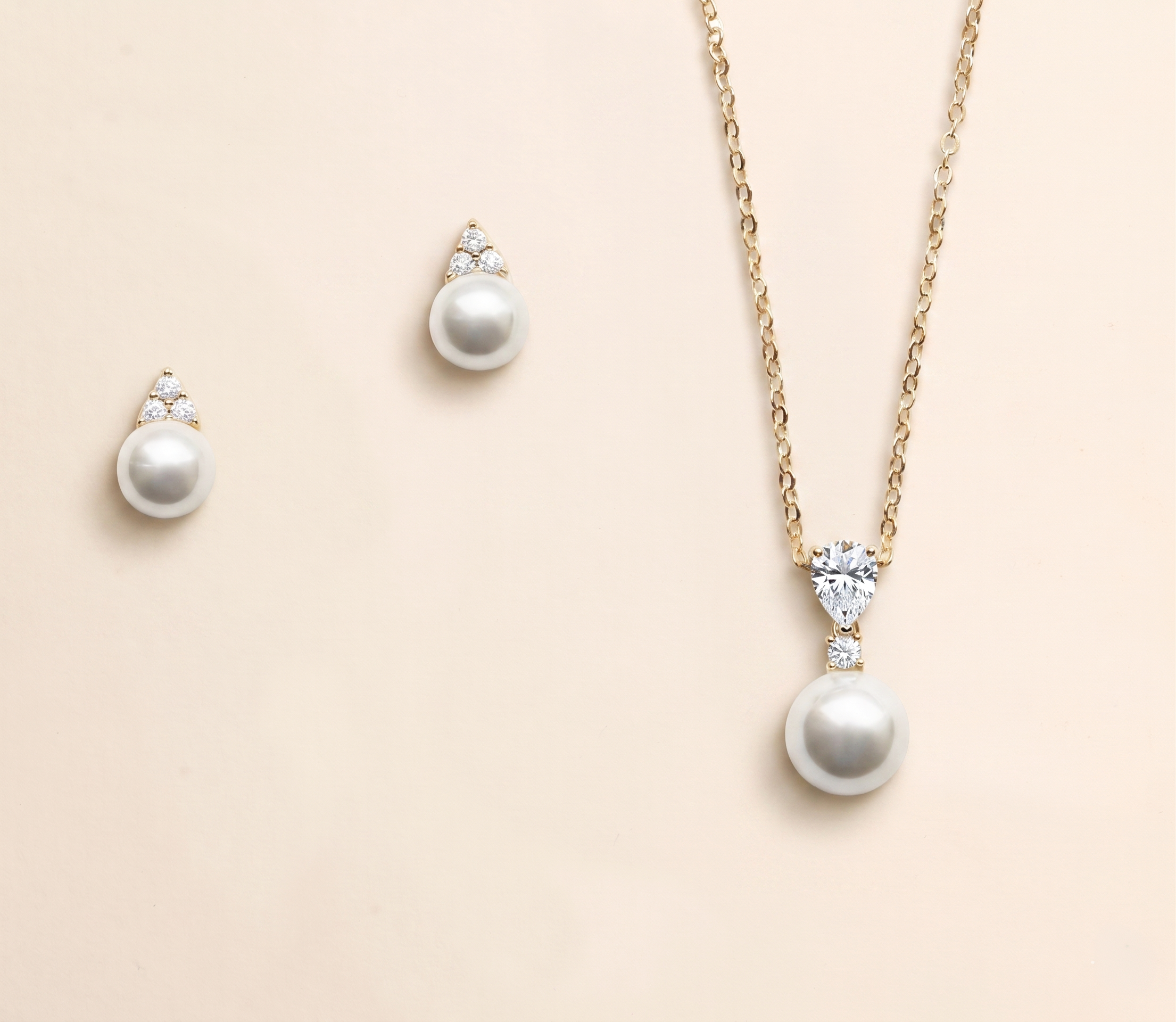 A necklace with a pendant and earrings made of pearls and diamonds against a light beige background.