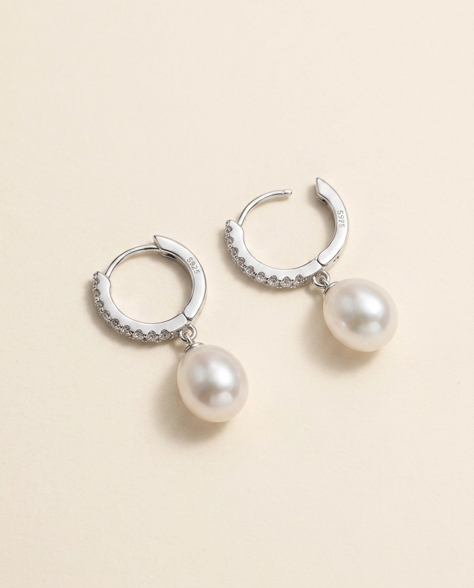 A pair of silver earrings with white pearls hanging from them.