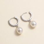 A pair of silver earrings with white pearls hanging from them.