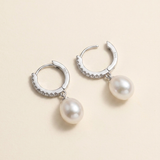 A pair of silver earrings with white pearls hanging from them.