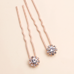 a pair of delicate, rose gold-colored hair clips adorned with small, clear gemstones.