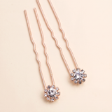 a pair of delicate, rose gold-colored hair clips adorned with small, clear gemstones.
