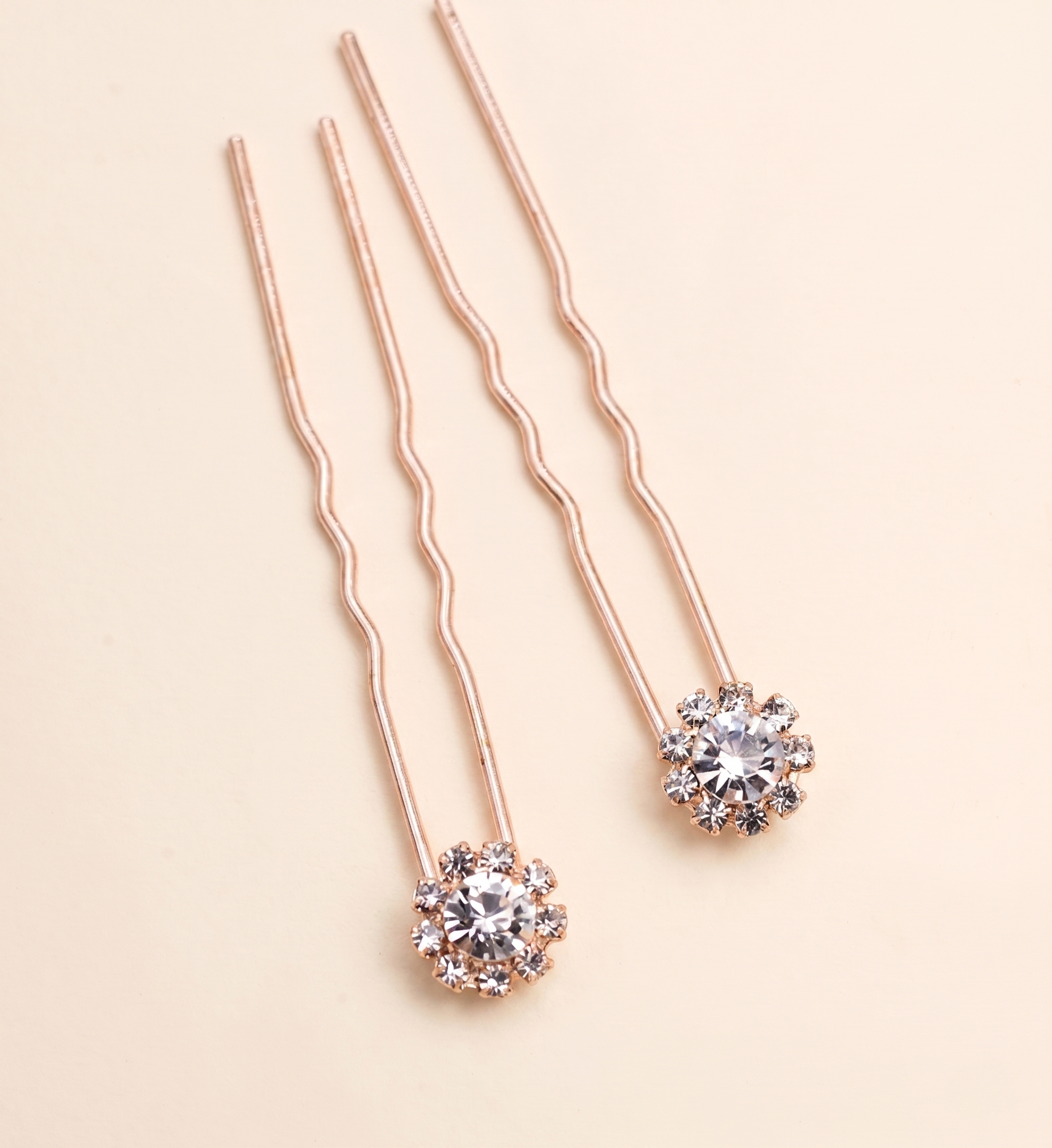a pair of delicate, rose gold-colored hair clips adorned with small, clear gemstones.