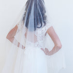 A woman wearing a white wedding dress with a long veil, standing against a plain white background.