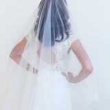 A woman wearing a white wedding dress with a long veil, standing against a plain white background.