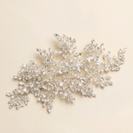 A decorative piece of jewelry with numerous small, sparkling crystal elements arranged in a floral or leaf-like design.