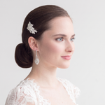 A woman with dark hair styled in a bun, wearing a white lace top and a diamond earring, looking off to the side with a thoughtful expression.
