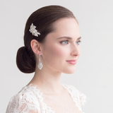 A woman with dark hair styled in a bun, wearing a white lace top and a diamond earring, looking off to the side with a thoughtful expression.