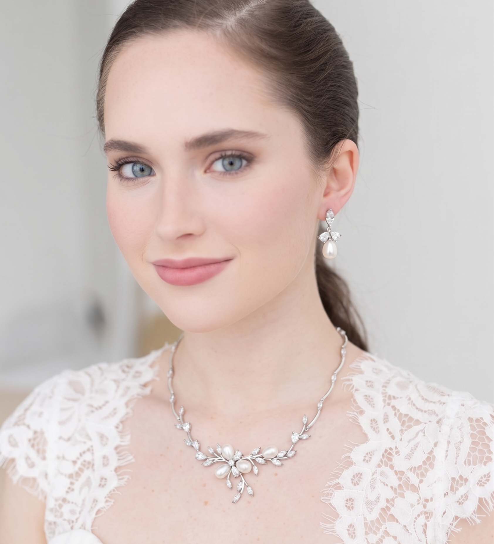 A woman wearing a white lace dress and a necklace with a floral design, smiling at the camera.