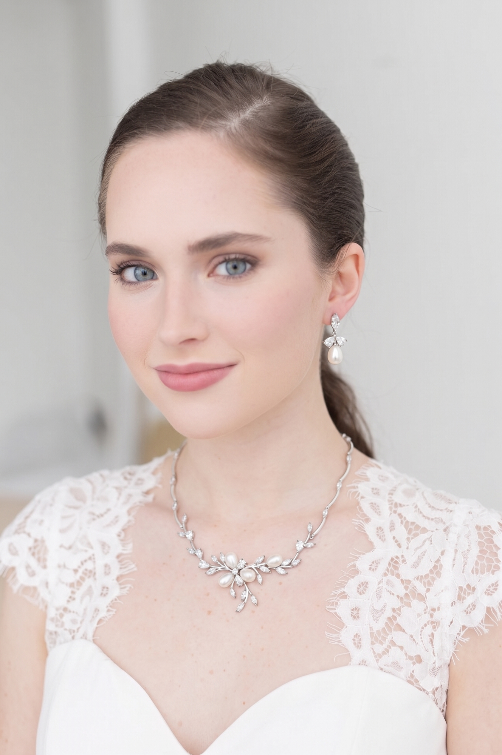 A woman wearing a white lace dress and a necklace with a floral design, smiling at the camera.