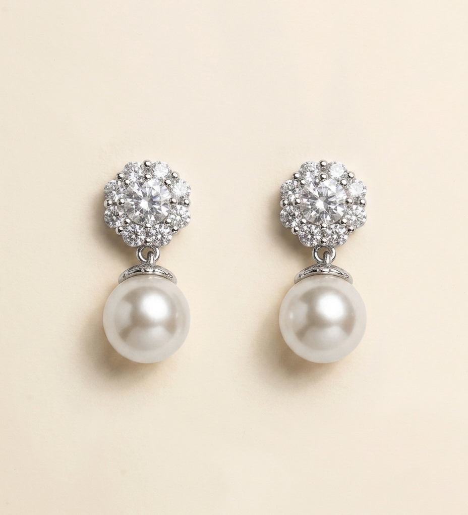 A pair of elegant earrings with a large, round pearl at the bottom and a cluster of smaller pearls on top, set against a light beige background.