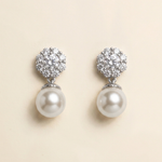 A pair of elegant earrings with a large, round pearl at the bottom and a cluster of smaller pearls on top, set against a light beige background.