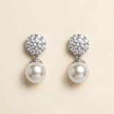 A pair of elegant earrings with a large, round pearl at the bottom and a cluster of smaller pearls on top, set against a light beige background.