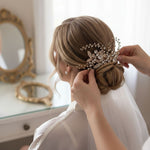 A person is styling a woman's hair with a decorative hairpiece, while the woman is wearing a white dress.