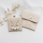 A beige jewelry box containing a necklace with three pearls and a matching beige pouch with the name "Emilly" printed on it.