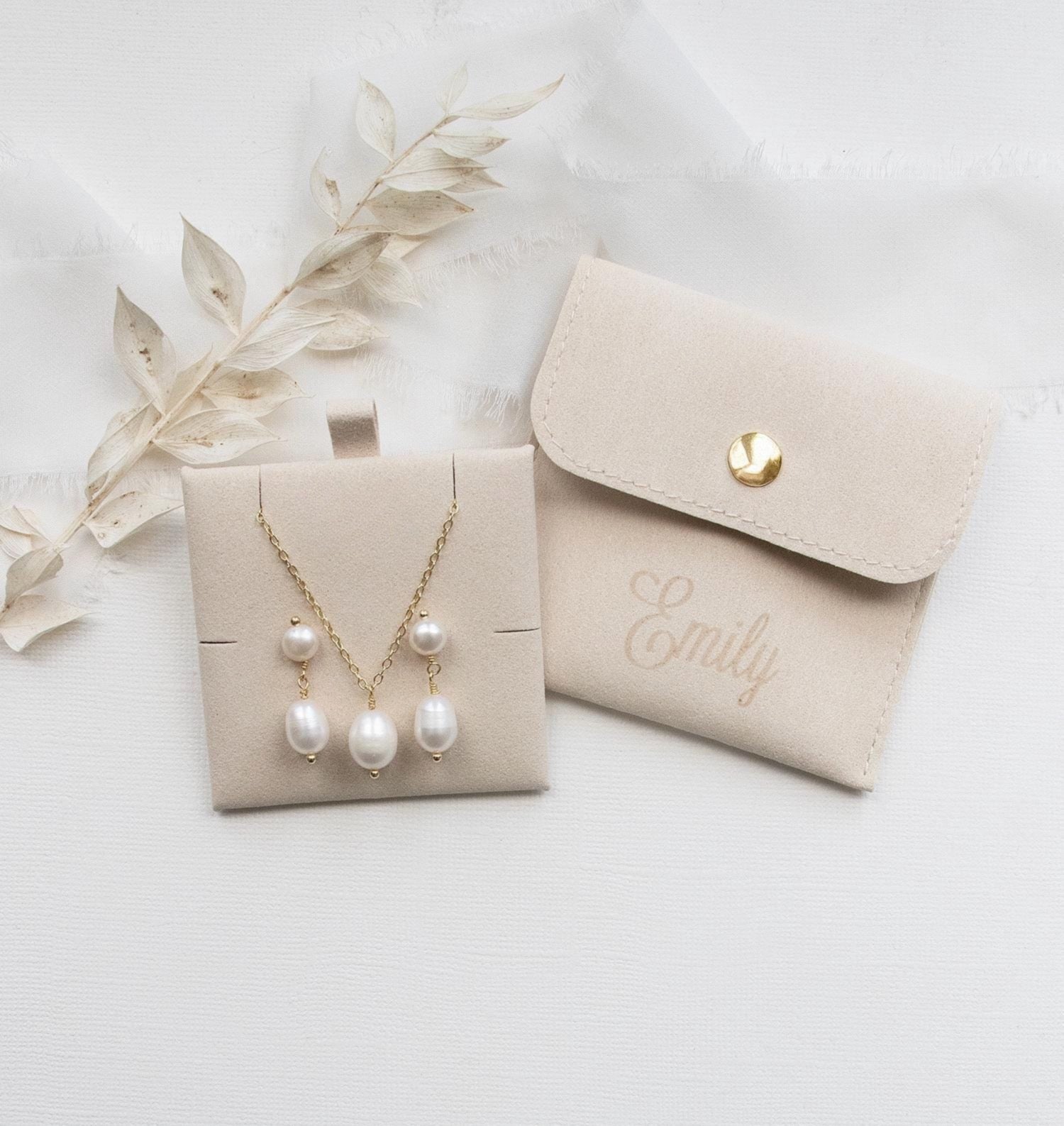 A beige jewelry box containing a necklace with three pearls and a matching beige pouch with the name "Emilly" printed on it.