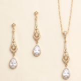 A set of three gold-colored jewelry pieces, including earrings and a necklace, with clear gemstones.