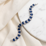 A bracelet with blue gemstones is displayed on a white marble surface.