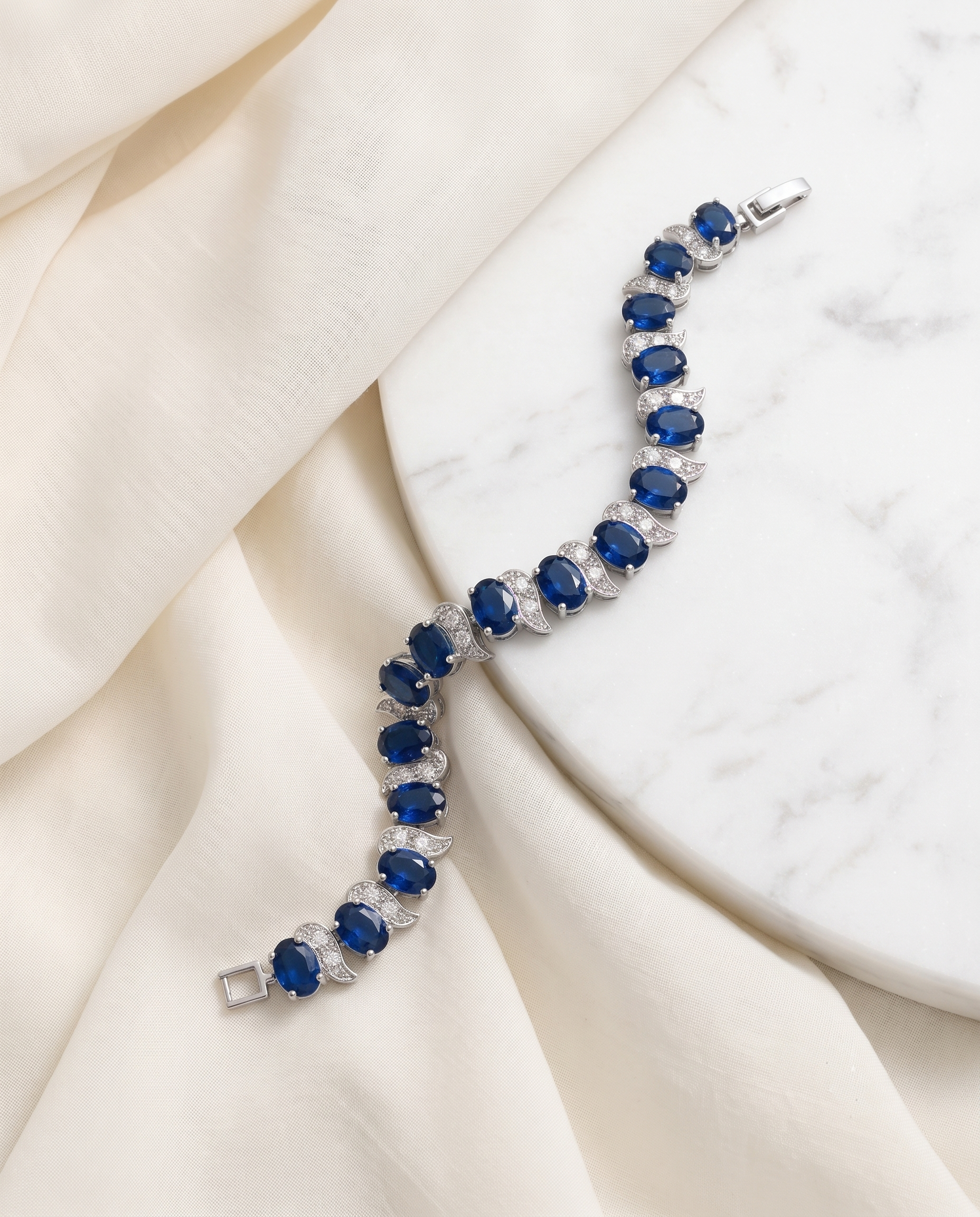 A bracelet with blue gemstones is displayed on a white marble surface.