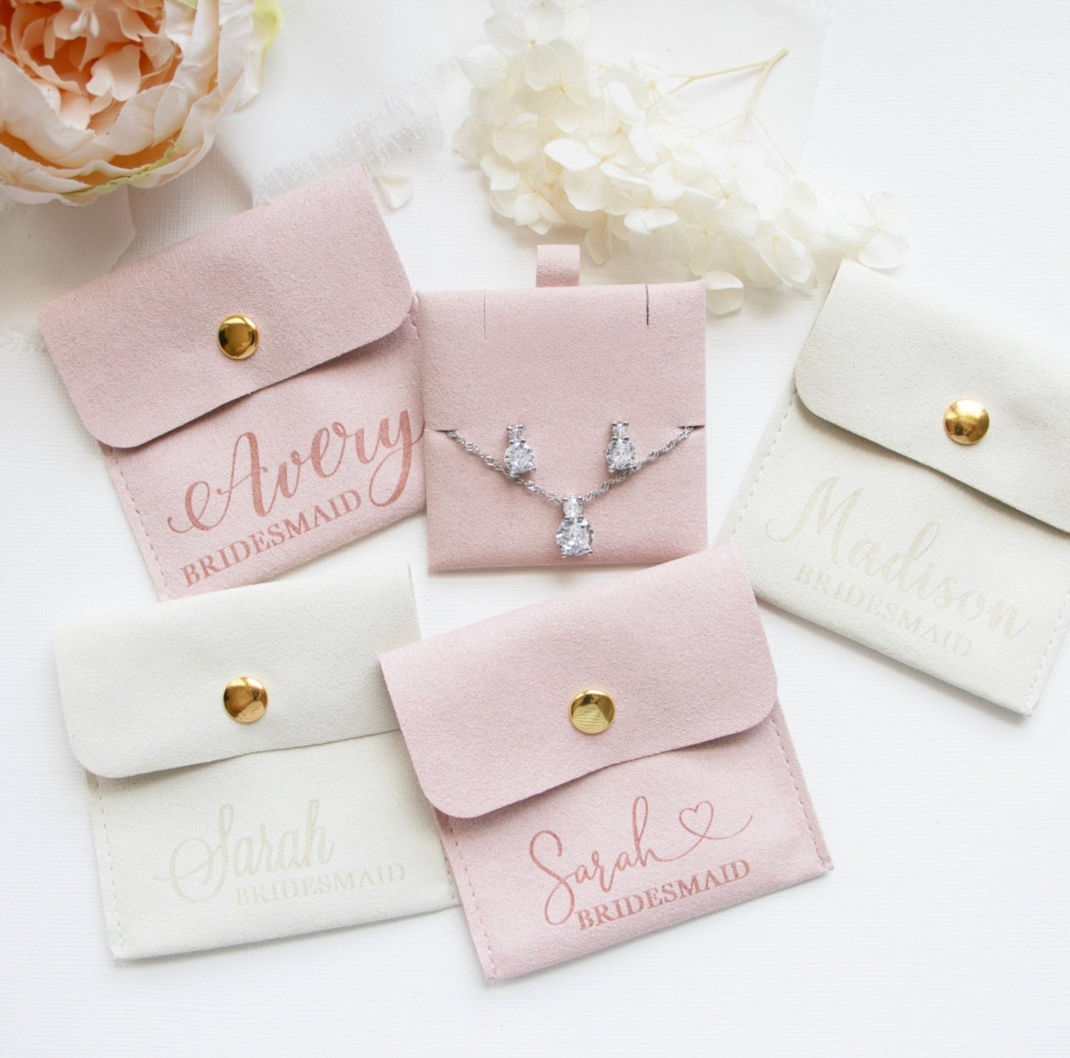 a collection of bridesmaid jewelry and accessories, including a necklace and earrings, all presented in pink and white fabric pouches or cases.