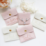 a collection of bridesmaid jewelry and accessories, including a necklace and earrings, all presented in pink and white fabric pouches or cases.