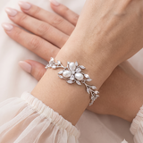 A close-up image of a person's hand wearing a bracelet with a floral design and a large crystal accent.
