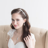 A young woman in a white wedding dress with a headband and earrings is posing for a portrait.