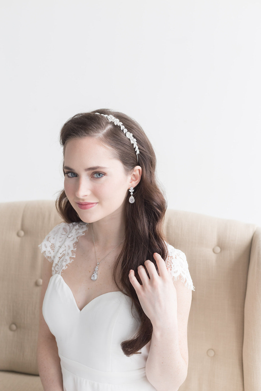 A young woman in a white wedding dress with a headband and earrings is posing for a portrait.