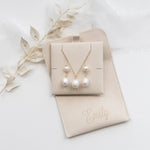 A beige jewelry box containing a necklace and earrings, with a personalized leather pouch labeled "Emilly" placed next to it.