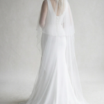 A woman in a long white wedding dress with a veil stands facing away from the camera, her back to the viewer.