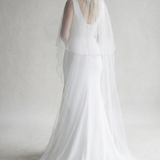 A woman in a long white wedding dress with a veil stands facing away from the camera, her back to the viewer.