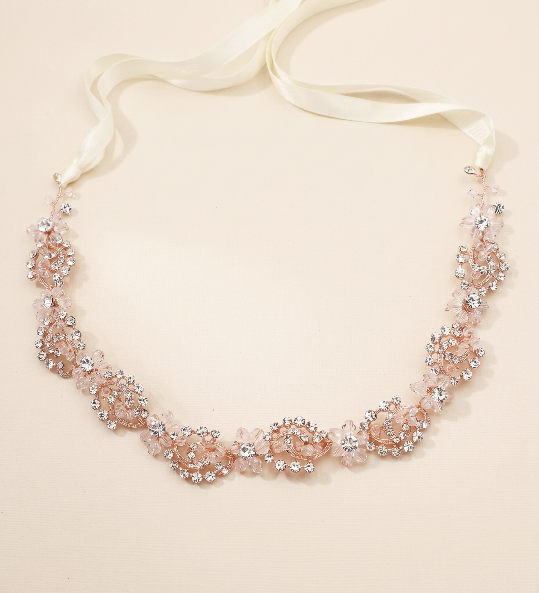 A delicate necklace with a white ribbon and a floral design made of small, clear, and pink-colored stones.