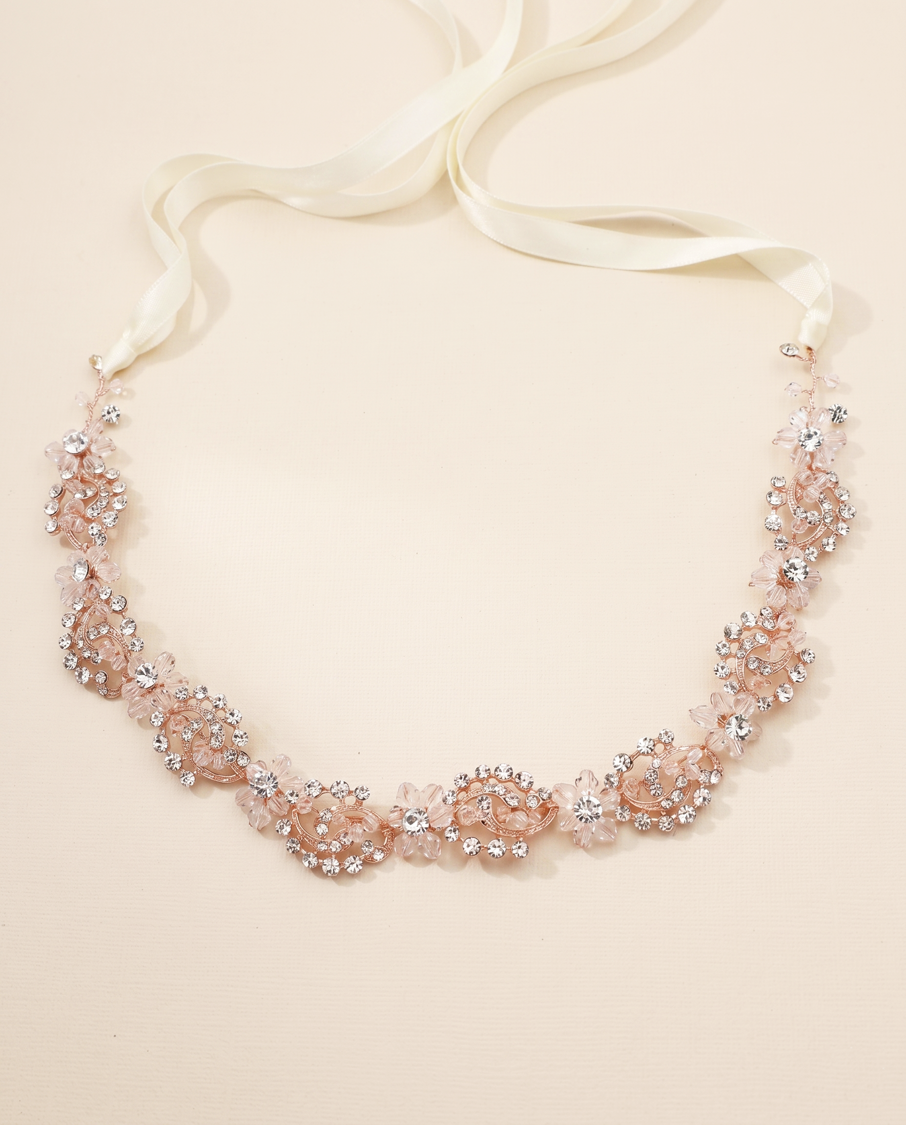 A delicate necklace with a white ribbon and a floral design made of small, clear, and pink-colored stones.