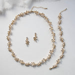 A delicate gold necklace with leaf-shaped pendants and earrings, along with a matching bracelet, are arranged on a white background.