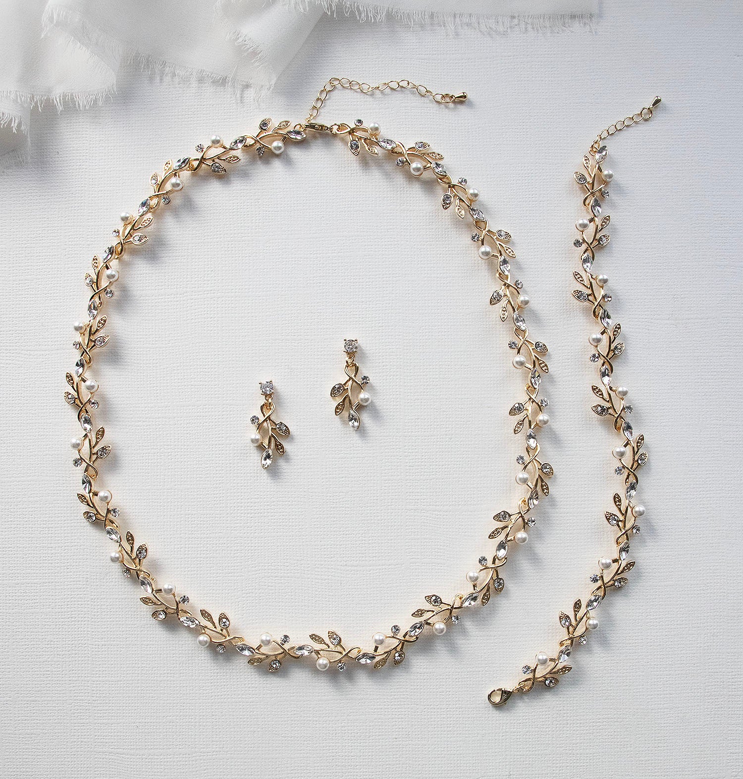 A delicate gold necklace with leaf-shaped pendants and earrings, along with a matching bracelet, are arranged on a white background.