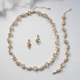 A delicate gold necklace with leaf-shaped pendants and earrings, along with a matching bracelet, are arranged on a white background.