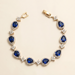 A gold bracelet adorned with blue gemstones, including diamonds, is displayed against a light background.