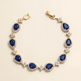 A gold bracelet adorned with blue gemstones, including diamonds, is displayed against a light background.