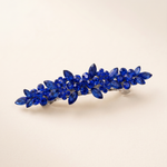 A decorative hair clip with blue gemstones arranged in a floral pattern.