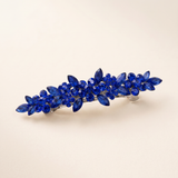 A decorative hair clip with blue gemstones arranged in a floral pattern.