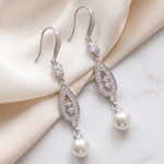 A pair of elegant earrings with pearls and diamonds resting on a white marble surface.
